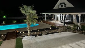 Een huis met een zwembad, een overdekt terras en een aangelegde tuin.