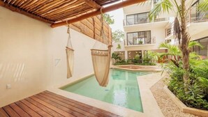 Ein Poolbereich mit Holzterrasse, Hängestühlen und einem Gebäude mit Balkonen und Pflanzen.