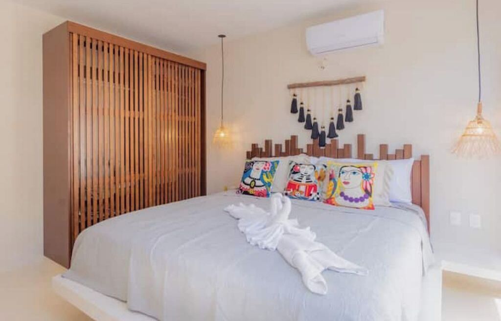 Une chambre d’hôtel avec un lit, une cloison en lattes de bois, un climatiseur fixé au mur et un luminaire suspendu.