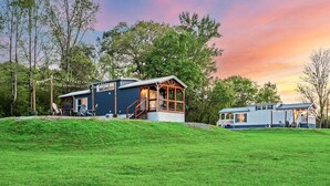 Eine Holzhütte mit einer Holzterrasse und einer Veranda, umgeben von üppiger Vegetation und Bäumen.