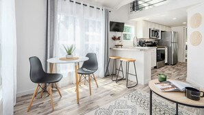 A modern kitchen with white cabinets, a stainless steel refrigerator, and a built-in oven. There is a dining area with a round table and two chairs. - Cozy Tiny Cabin Near Lake Guntersville (Guntersville)
