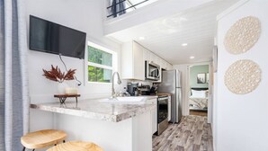 A modern kitchen with a flat-screen TV, wooden stools, and a large island. - Cozy Tiny Cabin Near Lake Guntersville (Guntersville)