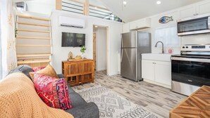Eine moderne Küche mit einem Edelstahl-Kühlschrank, Backofen und einer Mikrowelle. Ein Holztisch mit einer Pflanze und einem an der Wand befestigten Fernseher sind ebenfalls vorhanden.