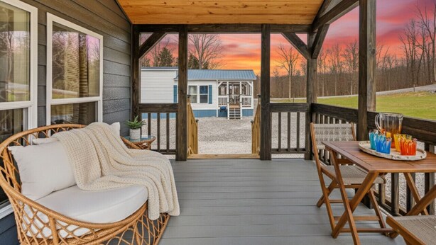 Eine überdachte Veranda mit einem Rattansofa und Tisch, Blick auf ein Haus und ein Sonnenuntergang im Hintergrund.