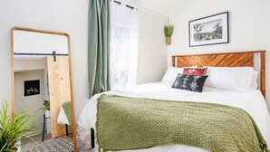 Ein Schlafzimmer mit einem hölzernen Bett, grünen Vorhängen, einem Spiegel, einem gerahmten Bild und einer kleinen Pflanze an der Wand.