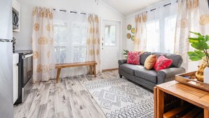 Ein modernes Wohnzimmer mit grauem Sofa, gemusterten Vorhängen, einer Holzbank und einem Esstisch mit einer Pflanze.