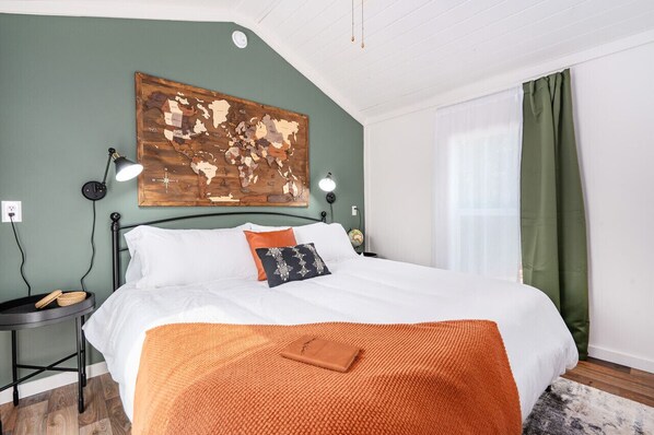 Un dormitorio con una cama, un cuadro de un mapa, una mesita de noche, una lámpara y una ventana con cortinas.