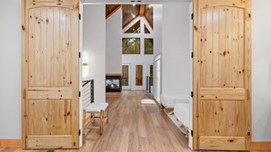 A spacious hallway with wooden doors leading to a living area with a fireplace, a bench, and a bed. - Mojave in the Pines - New Luxury Cabin in Hochatown Sleeps 4 (Broken Bow)