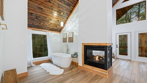 A spacious bathroom with a freestanding bathtub, a modern sink, and a large window offering a view of the forest. - Mojave in the Pines - New Luxury Cabin in Hochatown Sleeps 4 (Broken Bow)
