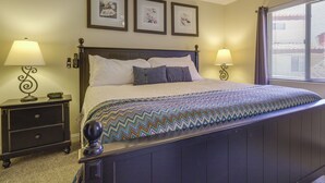 Una cama bien hecha con una colcha estampada, dos mesitas de noche con lámparas y tres cuadros enmarcados en la pared.