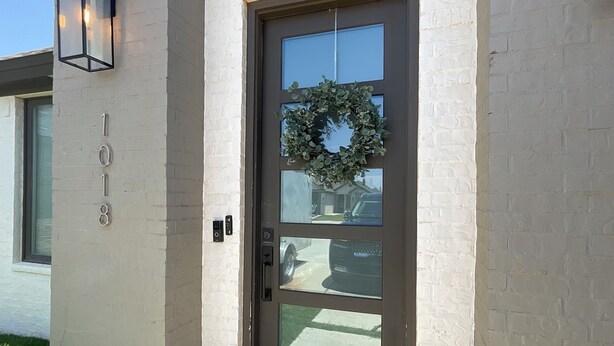 A modern house with a brown front door, a wreath, and a 'hey yall' mat.