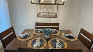 A dining table set with plates, napkins, and glassware, surrounded by wooden chairs.