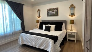 A bedroom with a bed, two bedside tables, a nightstand, a painting, and a mirror.