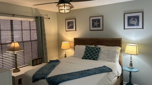 A hotel room with a bed, two bedside lamps, a ceiling fan, and framed pictures on the wall.