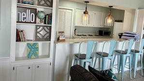 A kitchen with white cabinets, a bar area with blue chairs, and decorative shelves with books and a globe.