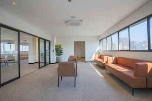 A modern interior with a long corridor, seating area with sofas, and large windows offering a city view.