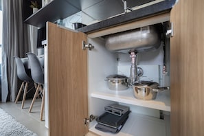 A compact kitchen with a built-in stove, a sink, and a shelf with pots.