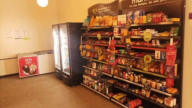 Interior de una tienda de comestibles con estantes llenos de diversos productos, un refrigerador y un congelador.