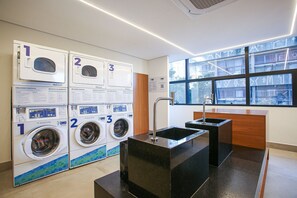 A laundry area with three washing machines, a sink, and a window with a view of buildings.