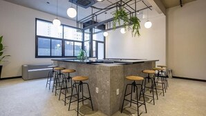 A modern kitchen with a central island, bar stools, hanging plants, and large windows. - VN Ueno (São Paulo)