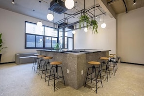 A modern kitchen with a central island, bar stools, hanging plants, and large windows. - VN Ueno (São Paulo)