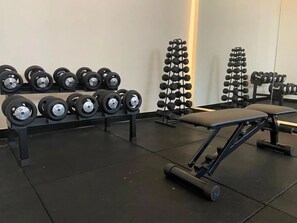 Un gimnasio con filas de mancuernas y discos de pesas, una banca y una estructura para sentadillas.