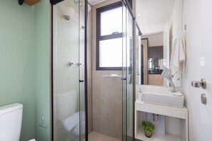 Un baño moderno con ducha de vidrio, lavamanos blanco y una pequeña planta en maceta.