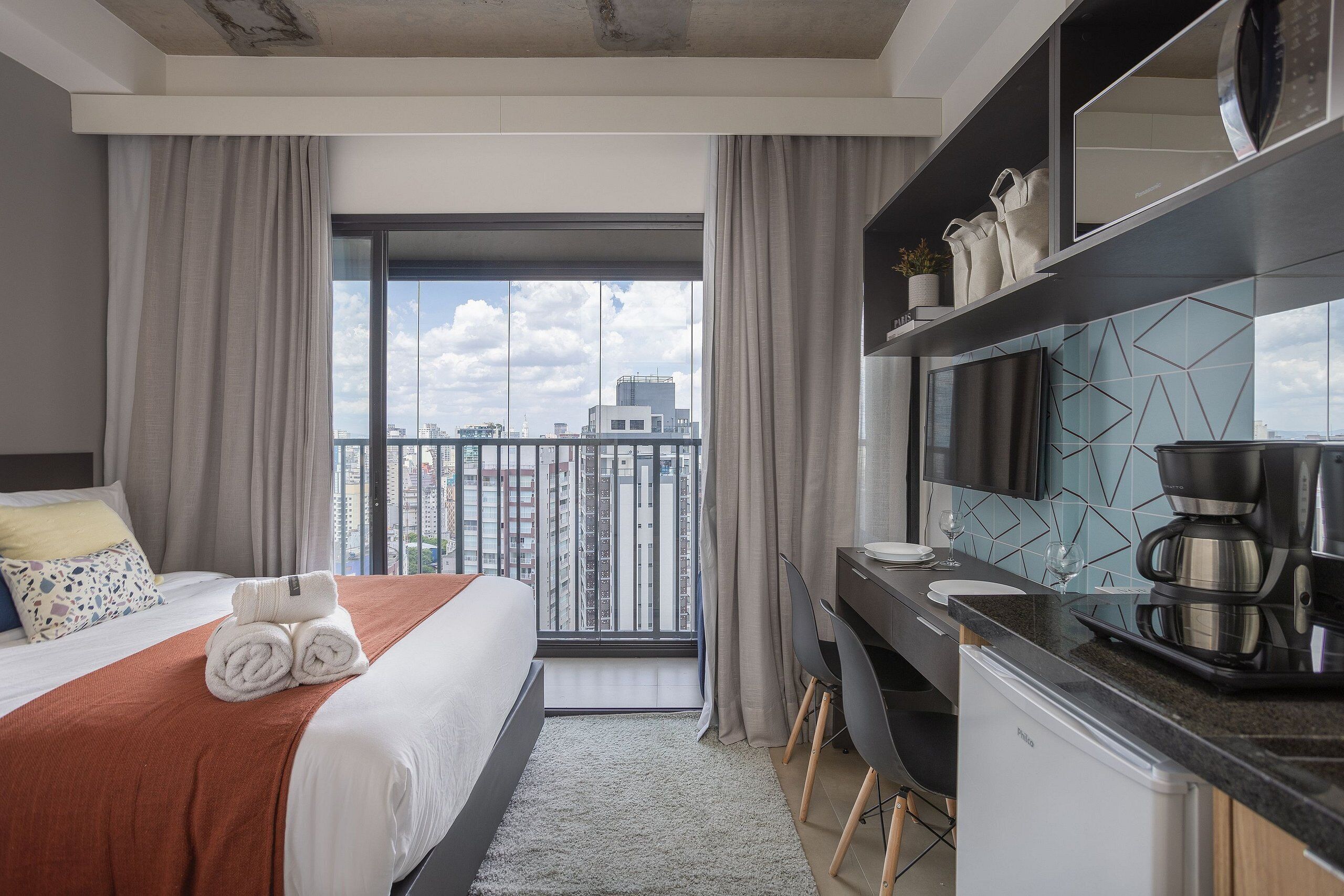 Een hotelkamer met een bed, een bureau, een koffiezetapparaat en uitzicht op de stad.