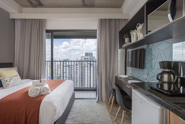 Habitación de hotel con cama, escritorio, cafetera y vistas a la ciudad.