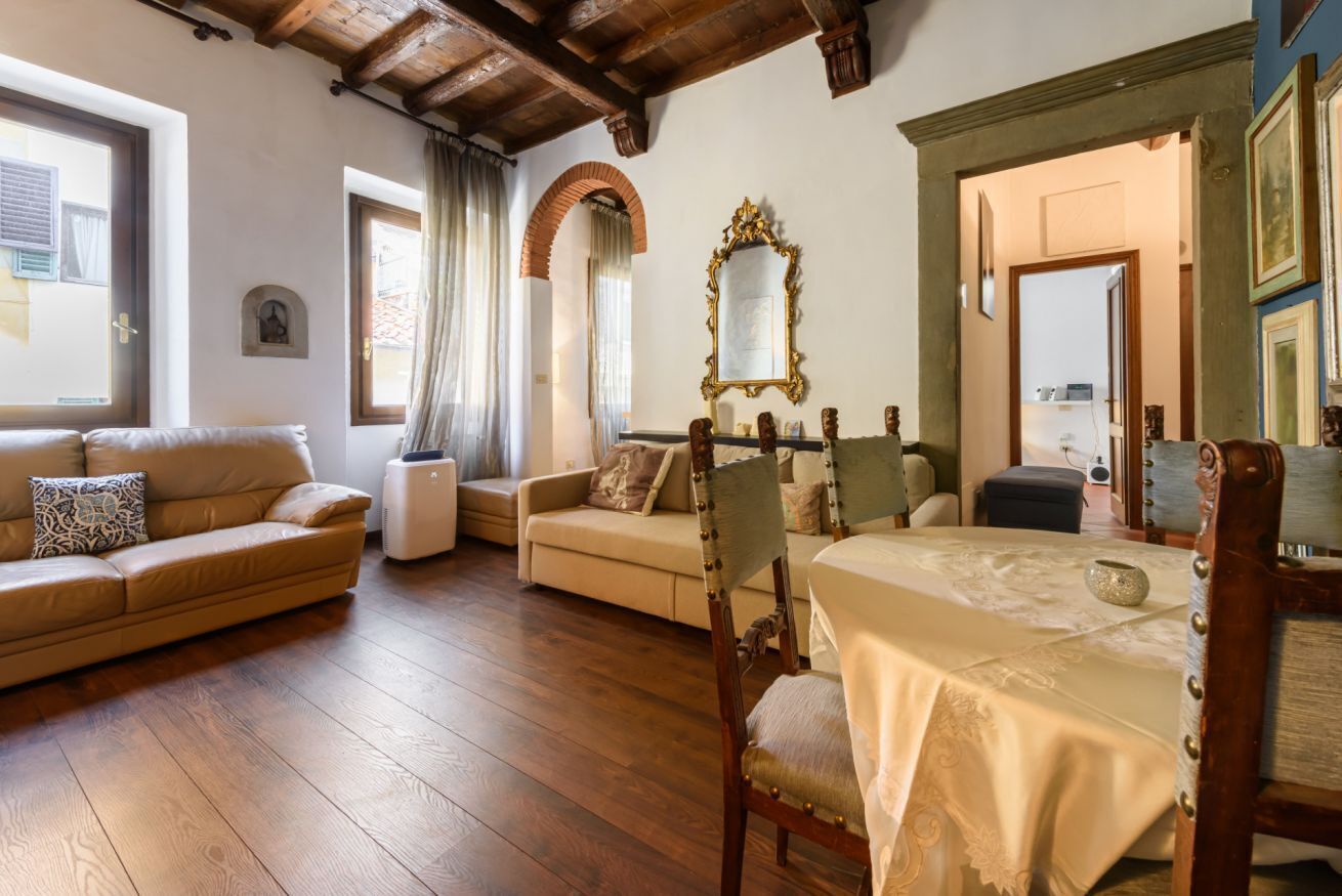 Un soggiorno arredato con pavimento in legno, un divano, una poltrona, un tavolo e uno specchio.
