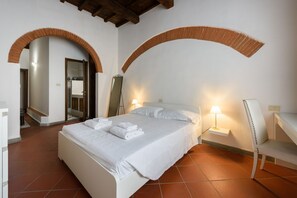 A bedroom with a bed, two bedside lamps, a chair, and an arched doorway.