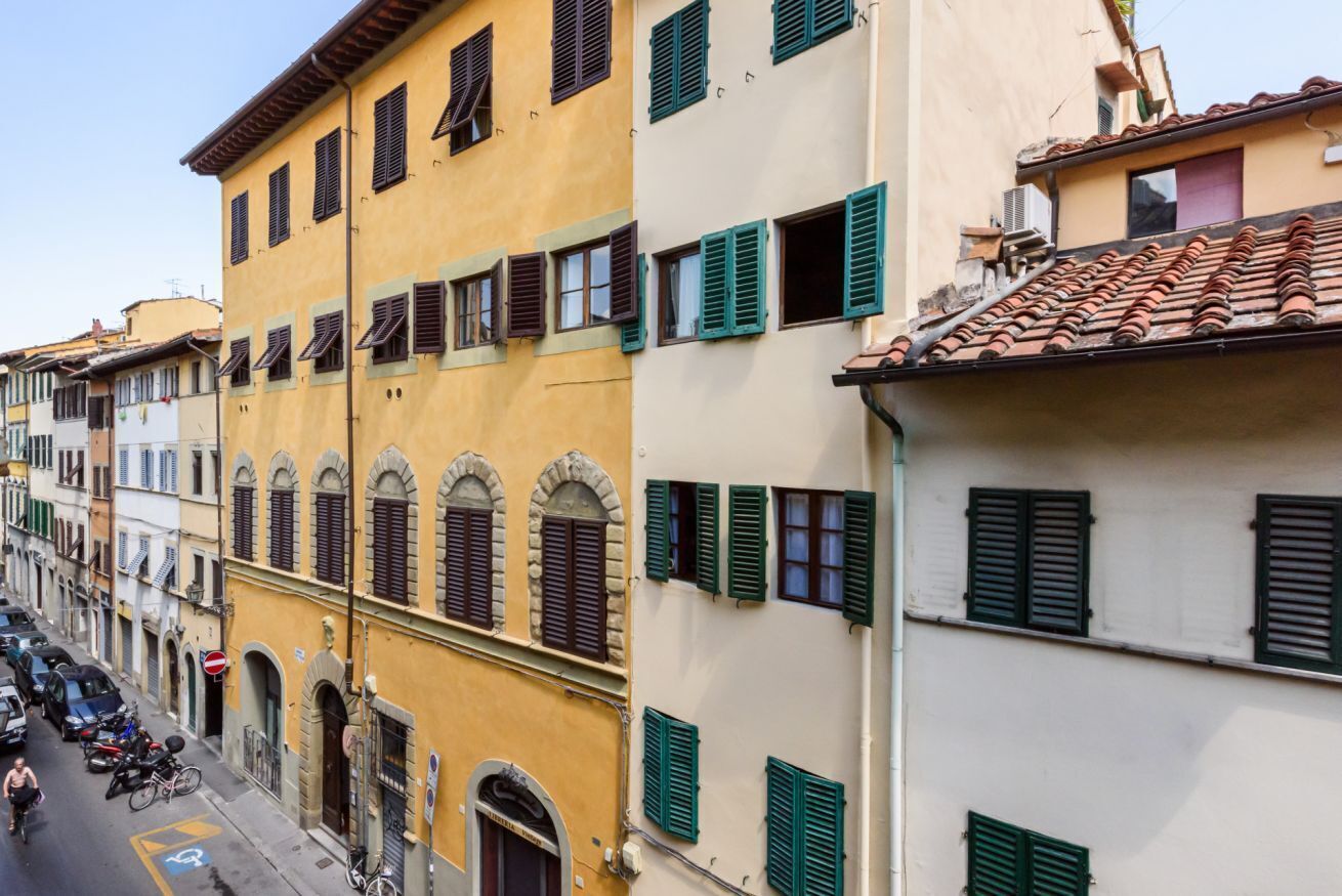 Una fila di edifici tradizionali con finestre ad arco e persiane, strada libera e veicoli parcheggiati.