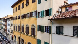 Una hilera de edificios tradicionales con ventanas arqueadas y contraventanas, una calle despejada y vehículos estacionados.