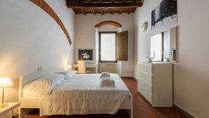 Un dormitorio con cama, mesita de noche, cómoda, ventana y un cuadro en la pared.