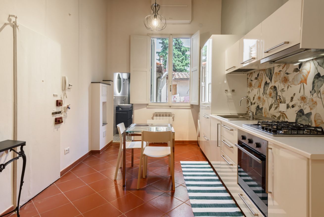 Una cucina compatta con tavolo e sedie, piano cottura e una finestra vista verde.