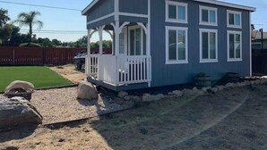Une petite maison à un seul étage, dotée d’un porche, d’une cour clôturée et surplombée d’un ciel dégagé.