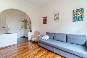 A living room with a grey sofa, wooden flooring, a patterned armchair, and wall art including a Picasso painting.
