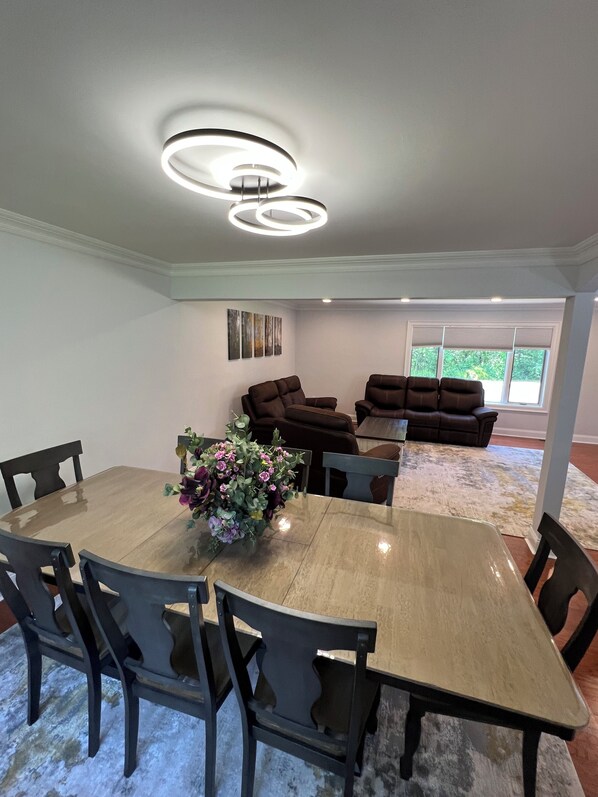 A dining area with a large wooden table and chairs, a floral centerpiece, and a ceiling light fixture.