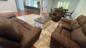 A spacious living room with brown leather sofas, a wooden coffee table, and a large rug. A dining area with a table and chairs is visible in the background. - Modern Getaway Retreat House on 2 Acres (Poughkeepsie)