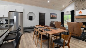 A modern kitchen with a built-in refrigerator, a dining area with a wooden table and chairs, a fireplace, and a view of the outdoors.