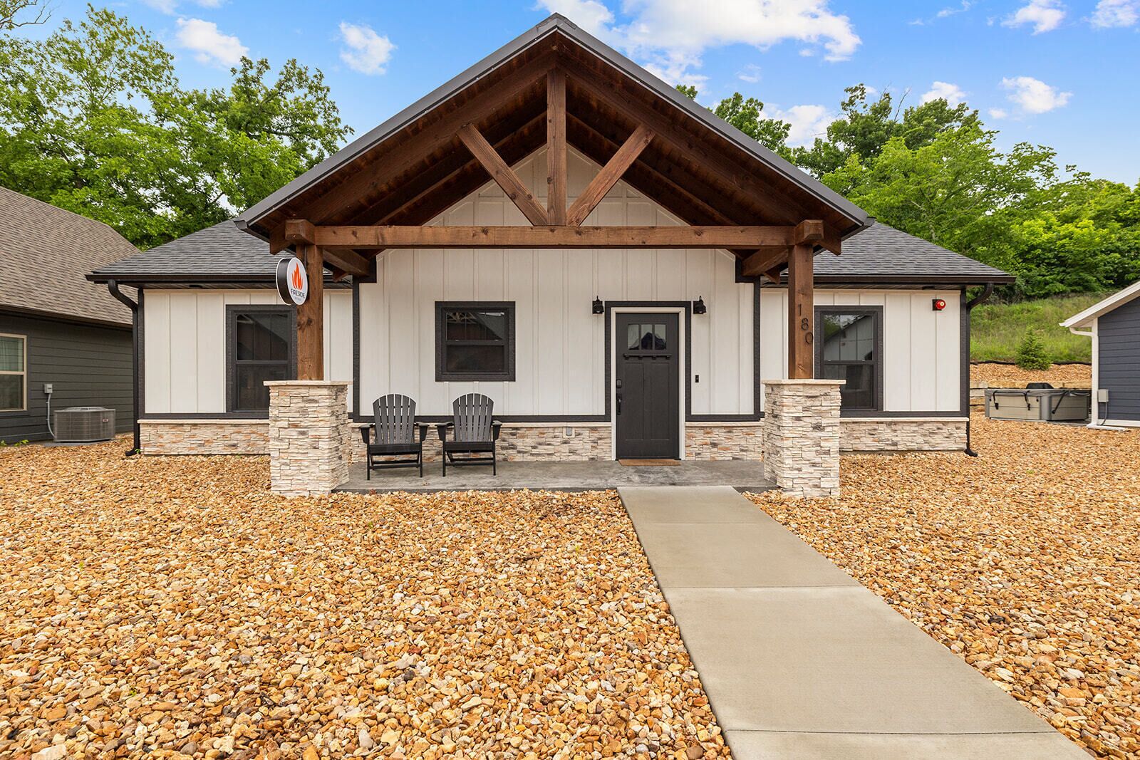 A building with a stone foundation, a wooden porch, and two Adirondack chairs.