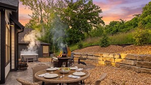 An outdoor patio with a round table set for dining, a grill, and a hot tub.