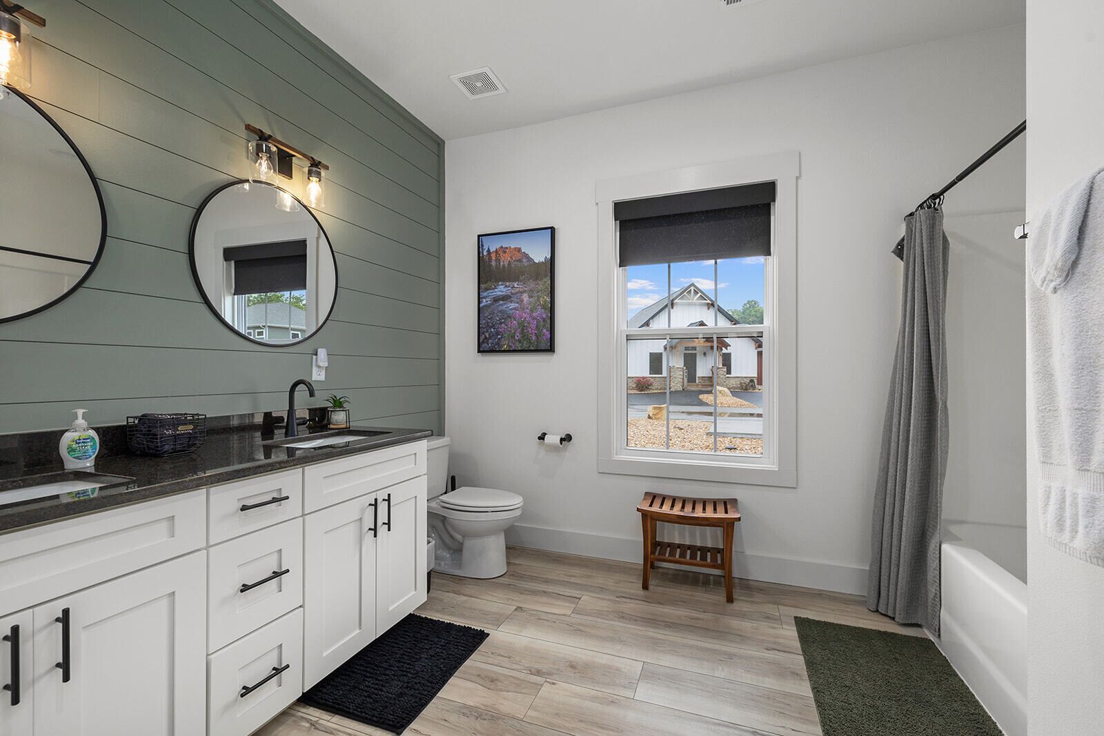 A bathroom with a toilet, sink, mirror, and a window with a view of a house.