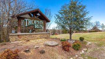 A wooden sign with "TROPHY RUN" written on it, surrounded by a stone wall, a tree, and a grassy area.