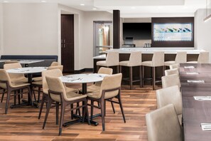 A modern dining area with round tables and chairs, a bar area with a flat-screen TV, and a kitchen in the background. - Residence Inn By Marriott Oklahoma City Norman (Norman)