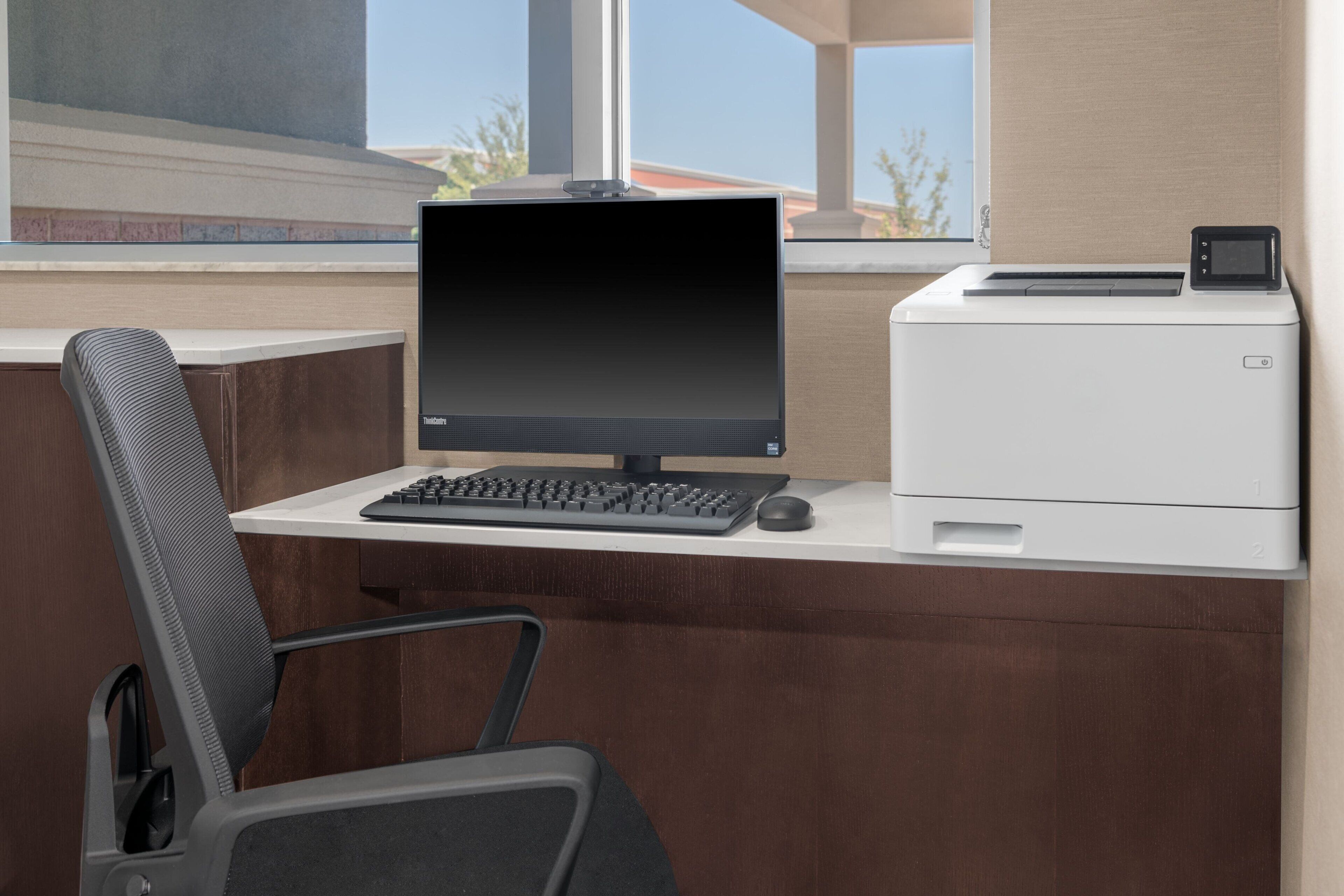 A modern office desk with a computer, keyboard, and mouse, a printer, and a chair.