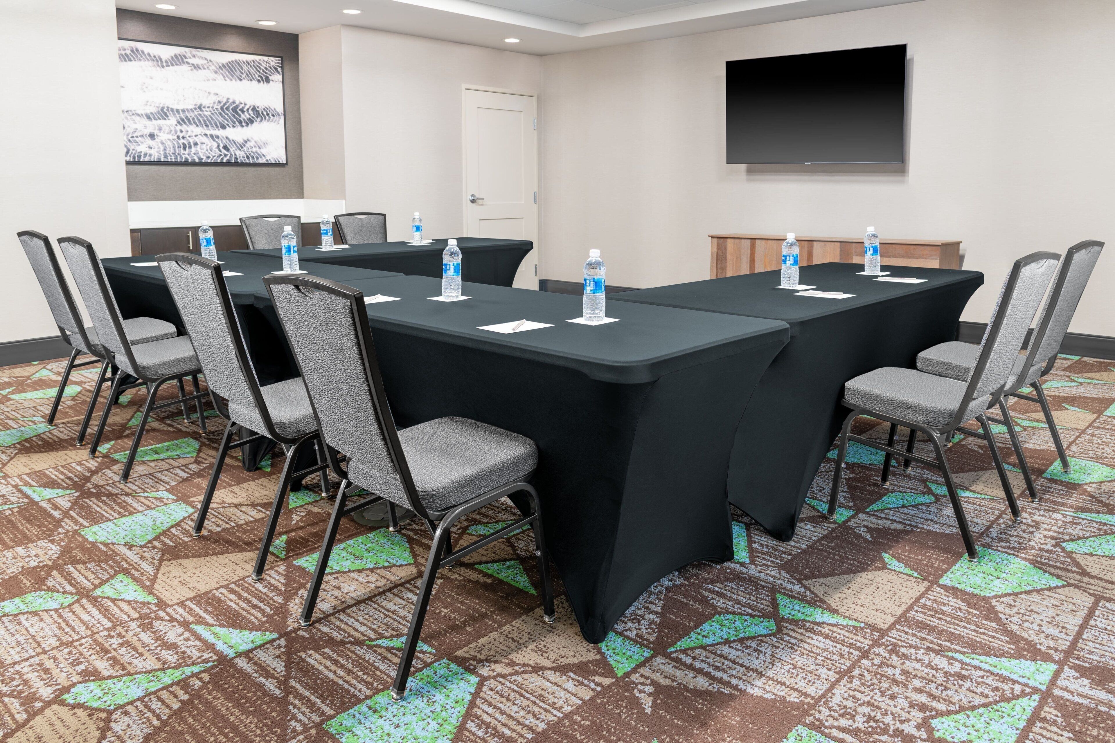 A conference room with a long table, chairs, water bottles, and a projector screen.