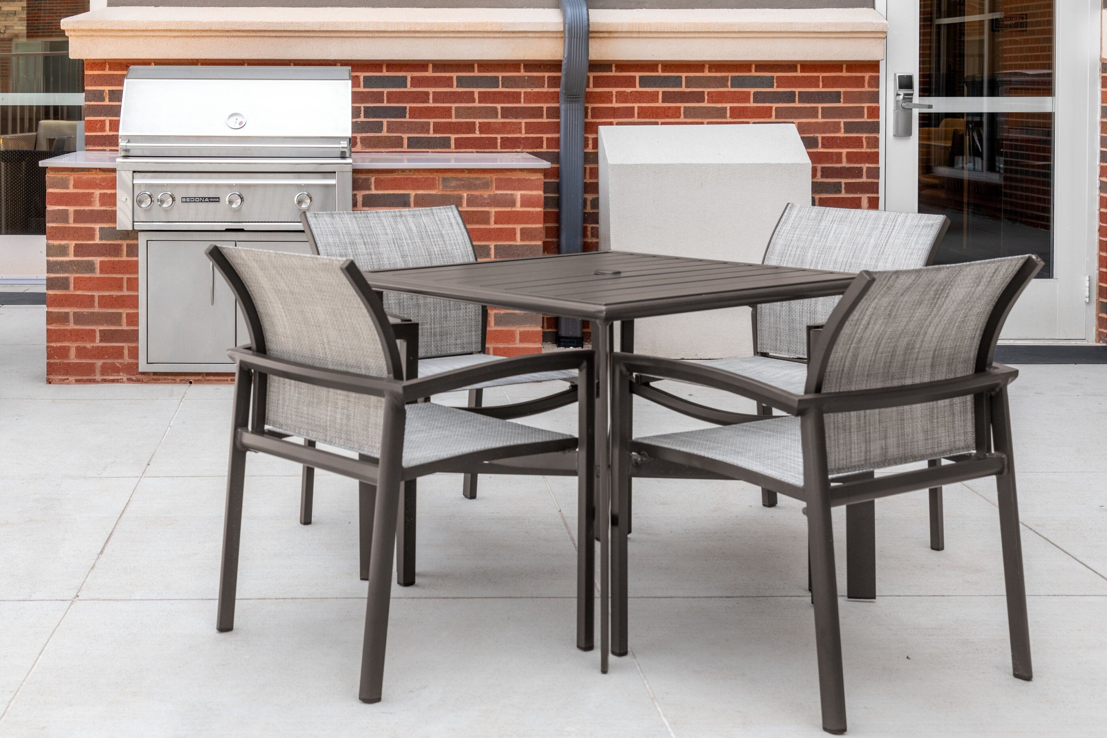 Une terrasse extérieure avec un mur en briques, un barbecue et quatre chaises avec des coussins.