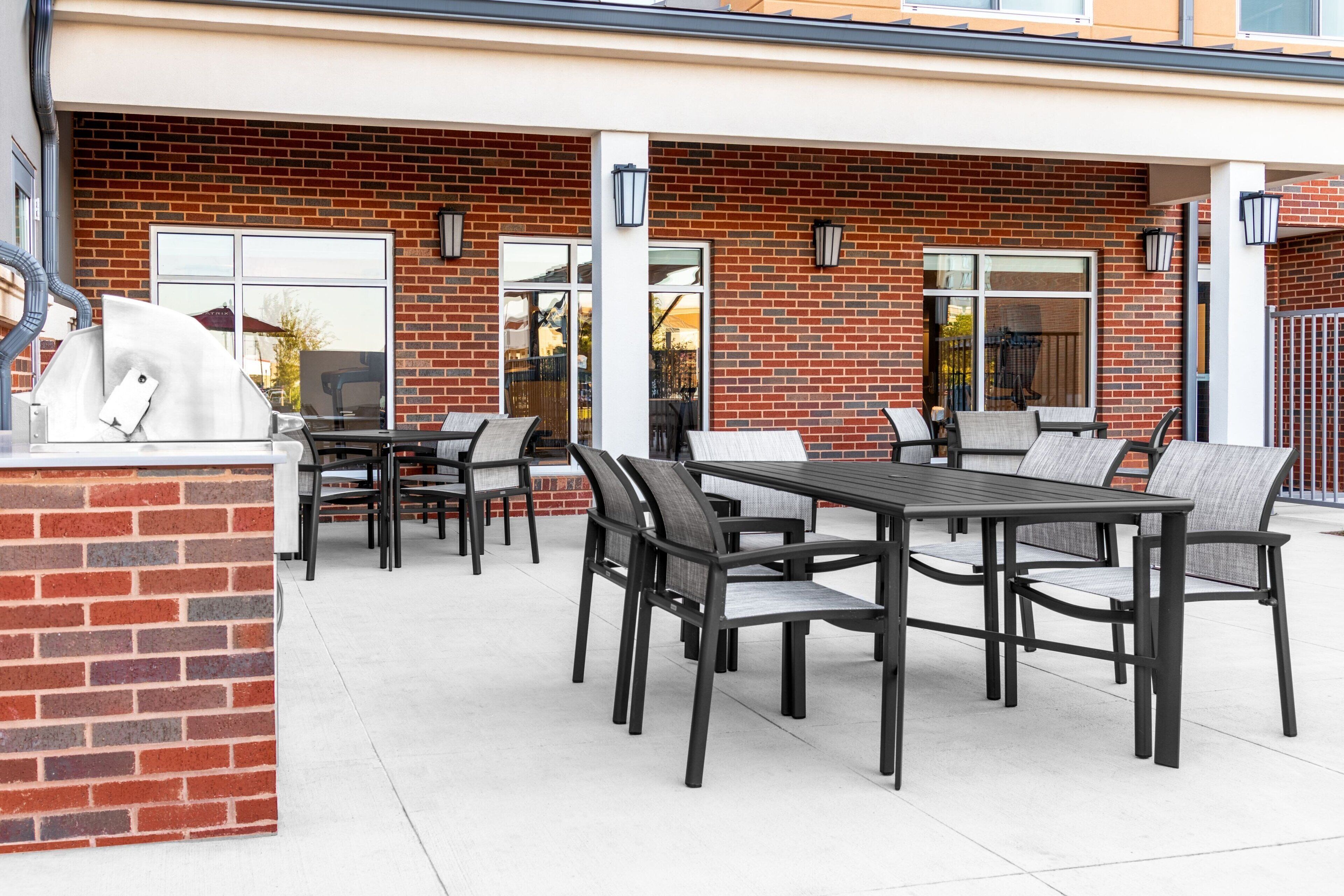 Un espace extérieur aménagé en terrasse, avec un mur en briques, un barbecue et plusieurs tables et chaises.