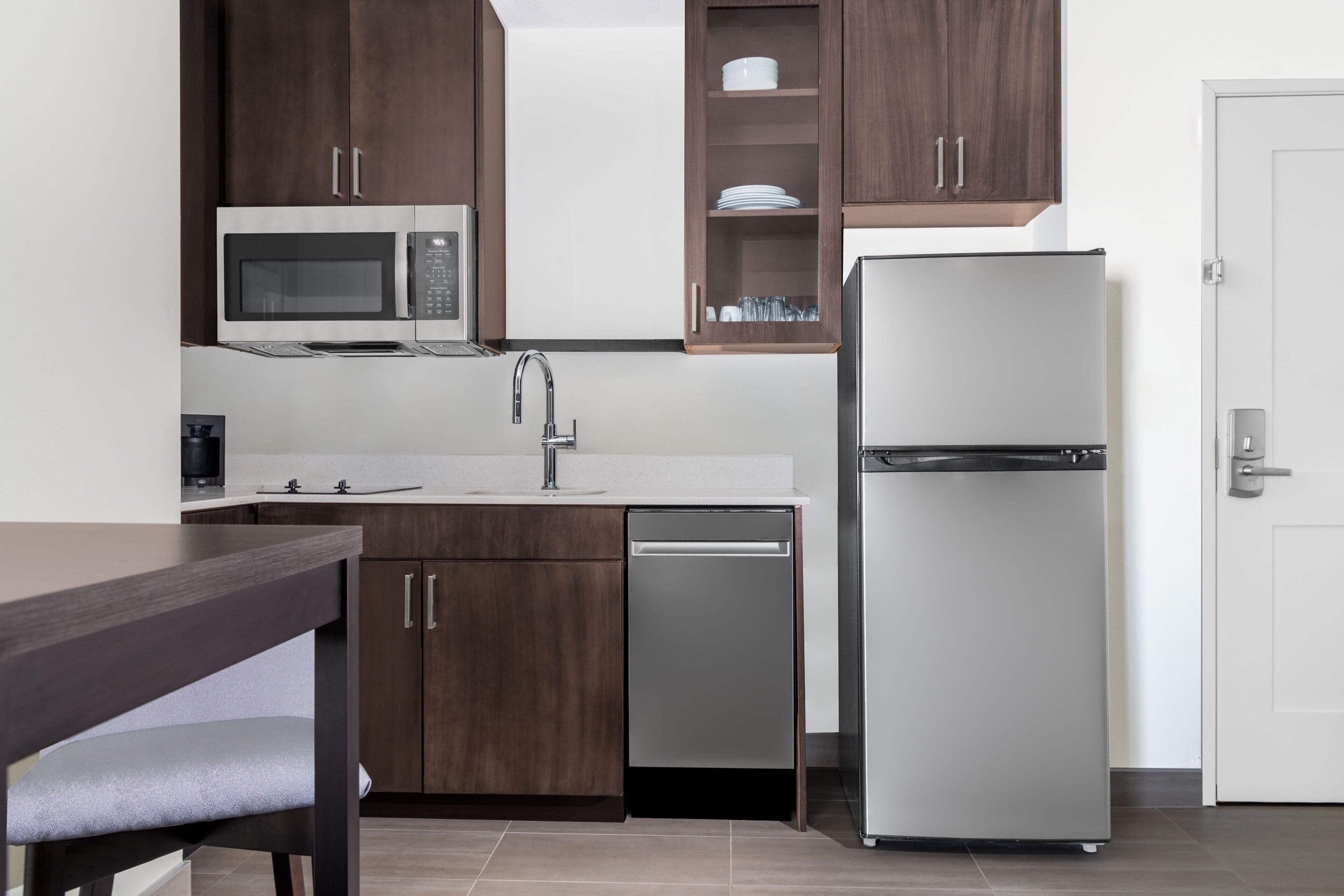A modern kitchen with dark wooden cabinets, a stainless steel refrigerator, a built-in microwave, and a dishwasher.